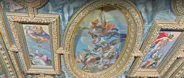 Foto di un soffitto decorato del Palazzo Ducale, caratterizzato da cornici dorate e dipinti. Al centro un grande affresco ovale con figure mitologiche, alcune alate, che sembrano ascendere verso il cielo tra le nuvole. Ai lati, altre scene dipinte, sempre incorniciate d'oro, rappresentano figure divine o eroi.