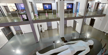 Spazio espositivo interno del Museo di Storia della Medicina. Al piano terra, un'installazione artistica a figura umana domina la scena, mentre ai piani superiori ci sono vetrine e pannelli informativi.