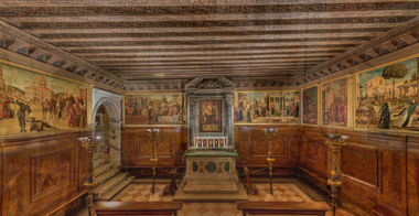 Interno della Scuola Dalmata dei SS. Giorgio e Trifone a Venezia. L'immagine mostra una sala caratterizzata da un soffitto ligneo a cassettoni, pareti affrescate e un altare riccamente decorato.