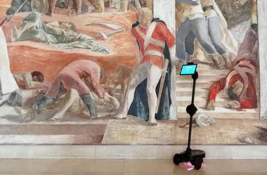 Foto del supporto robotico posizionato di fronte a un murale raffigurante una scena storica.