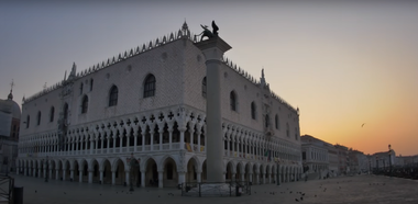 Facciata gotica di Palazzo Ducale illuminata dai primi raggi del sole, con la laguna sullo sfondo.