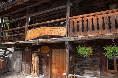 Foto della facciata d'ingresso in legno al Museo Etnografico, con un balcone decorato e una statua lignea all'ingresso.