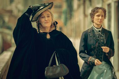 Riprese dalla protagonista che cammina lungo una fondamenta in abito nero tenedo con una mano il cappellino in testa