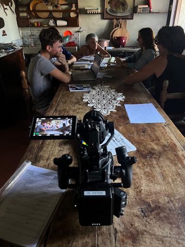 Set nella cucina di Villa Emo Capodilista: 4 personaggi seduti a tavola discutono tra di loro, in primo piano la macchina da presa