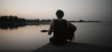 Filippo Francesco Centorame suona la chitarra seduto su un pontile del fiume al tramonto