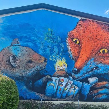 Murale di una volpe e una donnola che giocano alle carte trevisane da cui scaturiscono fantasmi di immagini di altri animali e una pira di carte