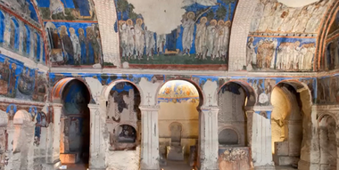 Interno di una chiesa rupestre in Cappadocia, con affreschi bizantini colorati raffiguranti scene bibliche e figure sacre.