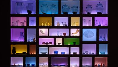 Vetrina museale con una vasta collezione di oggetti in vetro di diverse forme e colori, del Museo archeologico nazionale di Adria.