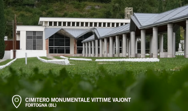 Veduta esterna del cimitero monumentale costruito in memoria delle vittime del Vajont, immerso nel verde. In basso, la scritta "Cimitero monumentale vittime Vajont. Fortogna (BL)".