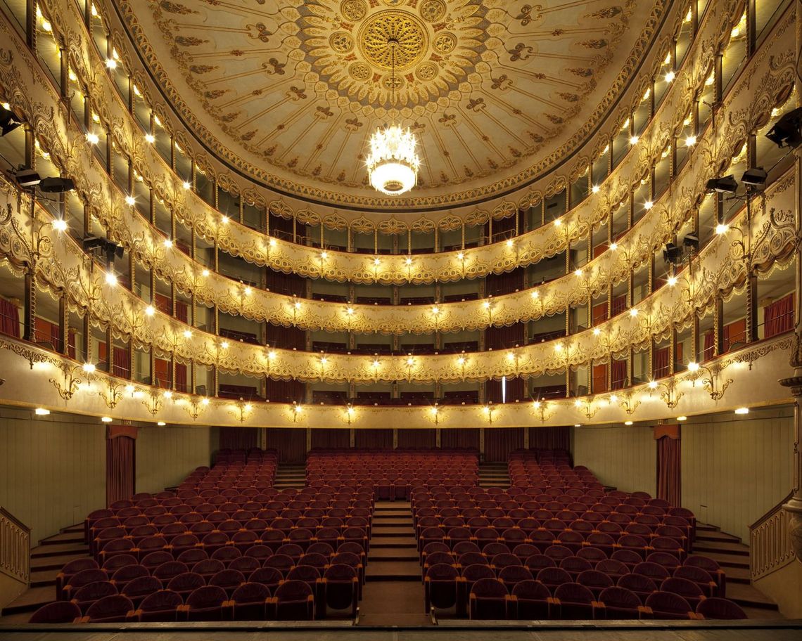 Vista dal palco della platea e delle quattro gallerie illuminate ed il soffitto finemente decorato con il lampadario acceso ed in stile con la sala