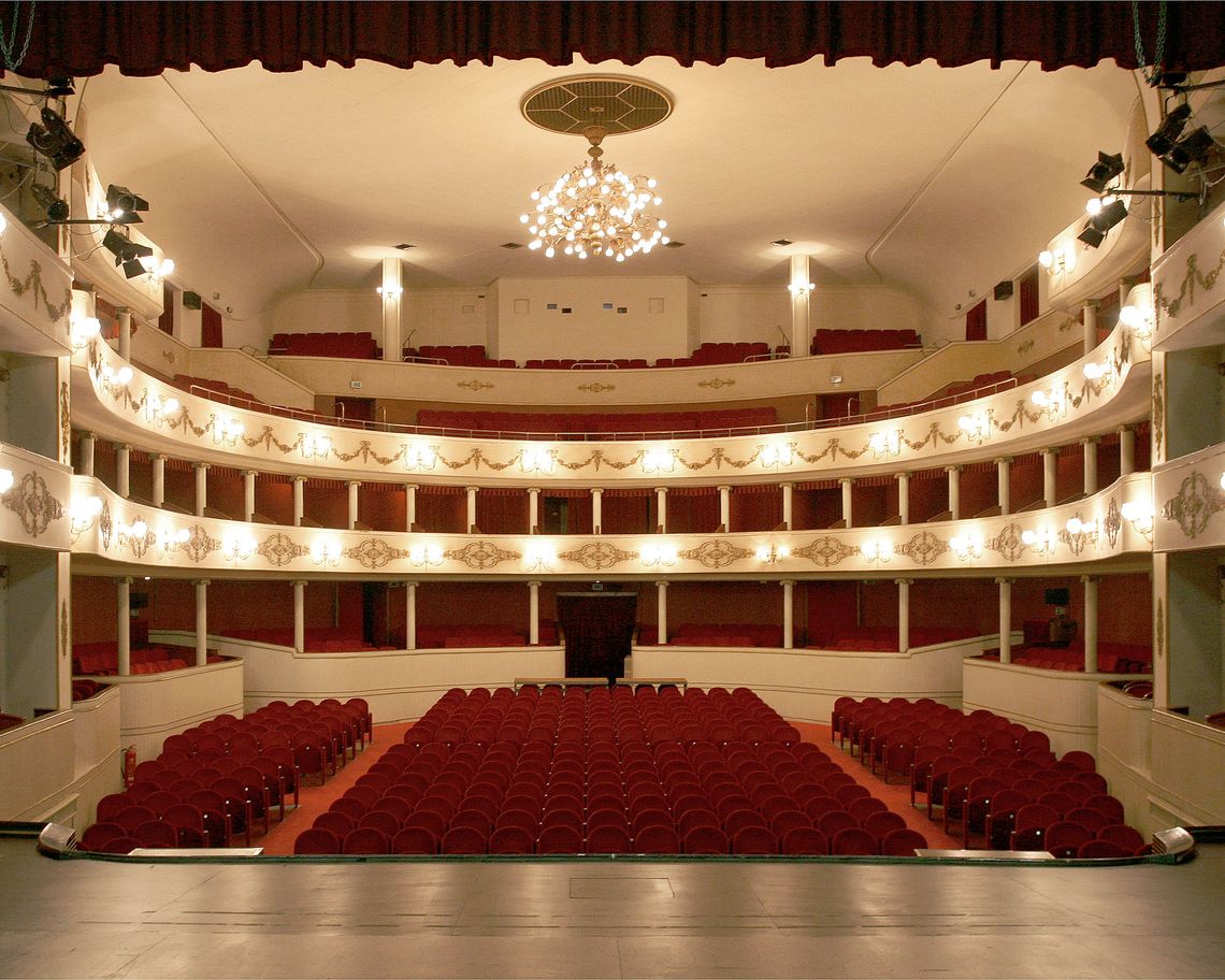 Vista dal palco della platea con poltroncine rosse e delle due gallerie illuminate ed il loggione