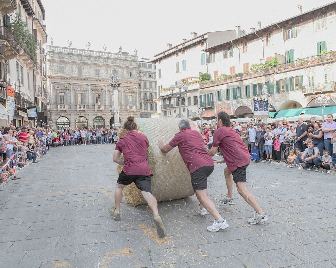 una donna e due uomini fanno rotolare una grande balla di fieno