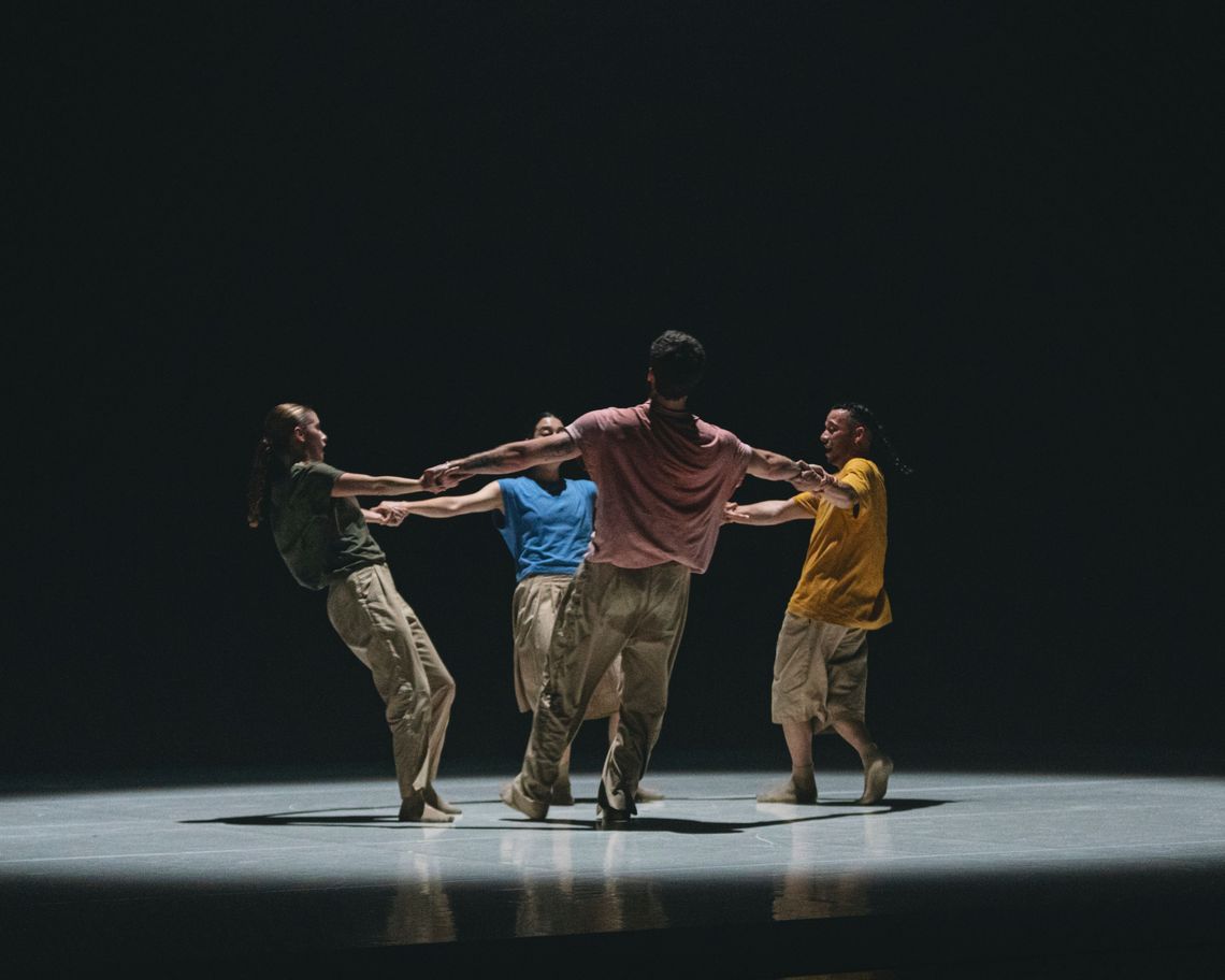 quattro danzatori in cerchio con le braccia allungate si tengono per mano