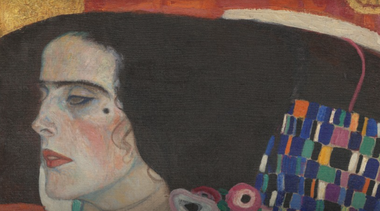 Particolare dall'opera Giuditta II di Klimt, che ritrae una donna con i capelli neri, un cappello e un abito decorato con motivi geometrici colorati. Lo sfondo è rosso e oro.