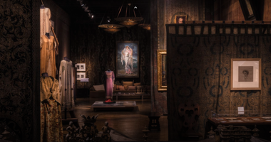 Foto dell'interno di Palazzo Fortuny. Le pareti sono rivestite da preziosi tessuti, mentre al centro della sala si trovano manichini che indossano abiti storici.