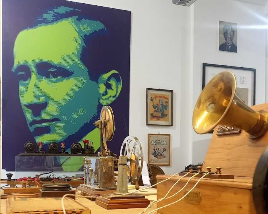 tavolo con strumenti scientifici e pannello con foto di Guglielmo Marconi in verde e nero