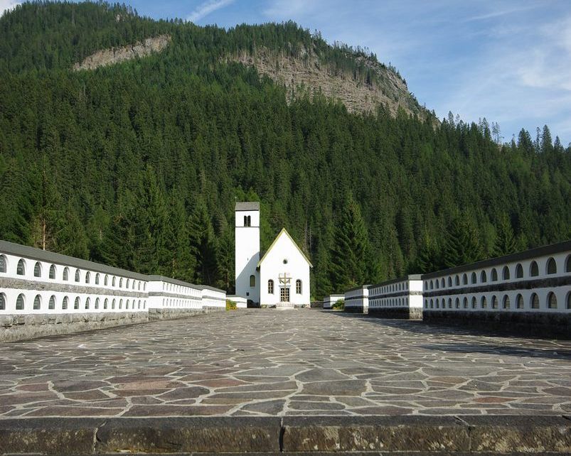 veduta frontale del sacrario con due file di ossari e chiesetta sul fondo