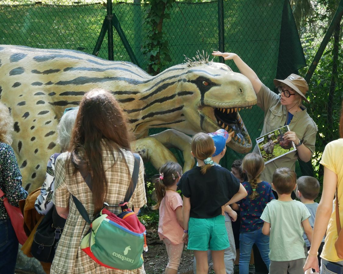 Dinosauro a grandezza naturale con guida che spiega e bambini ed adulti di spalle