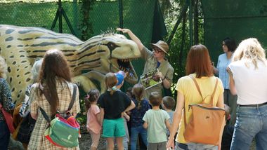 Dinosauro a grandezza naturale con guida che spiega e bambini ed adulti di spalle