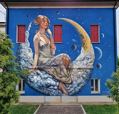 Murale sulla parete di una scuola con sfondo blu e donna seduta su una mezza luna. La figura è Pasitea, una delle Grazie della mitologia greca, circondata da stelle e pianeti. Indossa un semplice abito chiaro stile greco antico e i capelli lisci raccolti. Ha gli occhi socchiusi come se stesse per addormentarsi ed è seduta appoggiata con la mano sinistra per tenersi dritta.