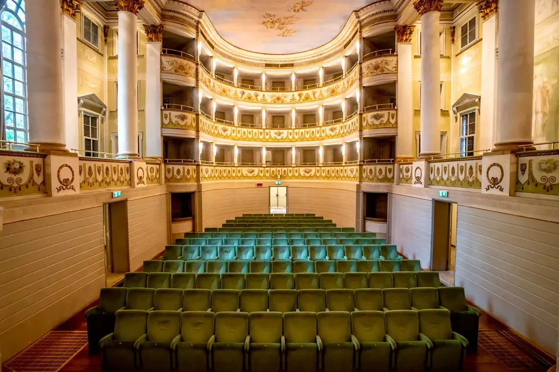 Foto della platea del teatro accademico di castelfranco veneto con decorazioni in oro e mura bianche, illuminate da luci calde.