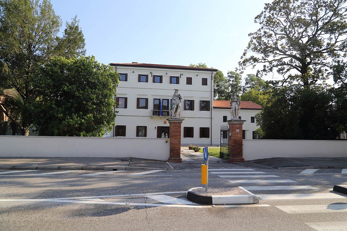 Edificio esterno della Biblioteca: villa bianca a tre piani immersa in un grande giardino con ingresso con due statue