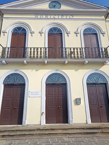 Palazzo storico di due piani di colore giallo pallido. Al piano terra e al primo piano tre finestrone ad arco chiuse da balconi marroni. Tetto a timpano.