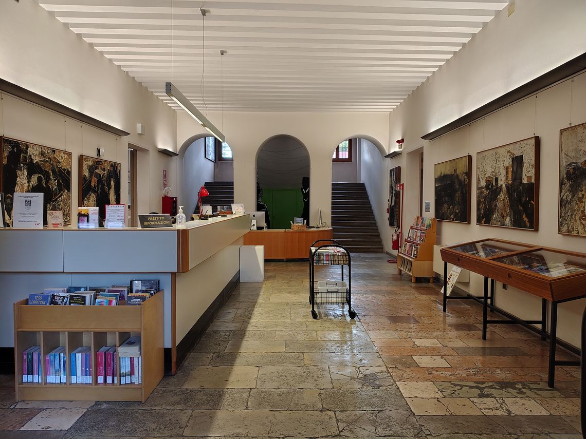 ingresso della biblioteca con bancone e scaffali, archi e scale